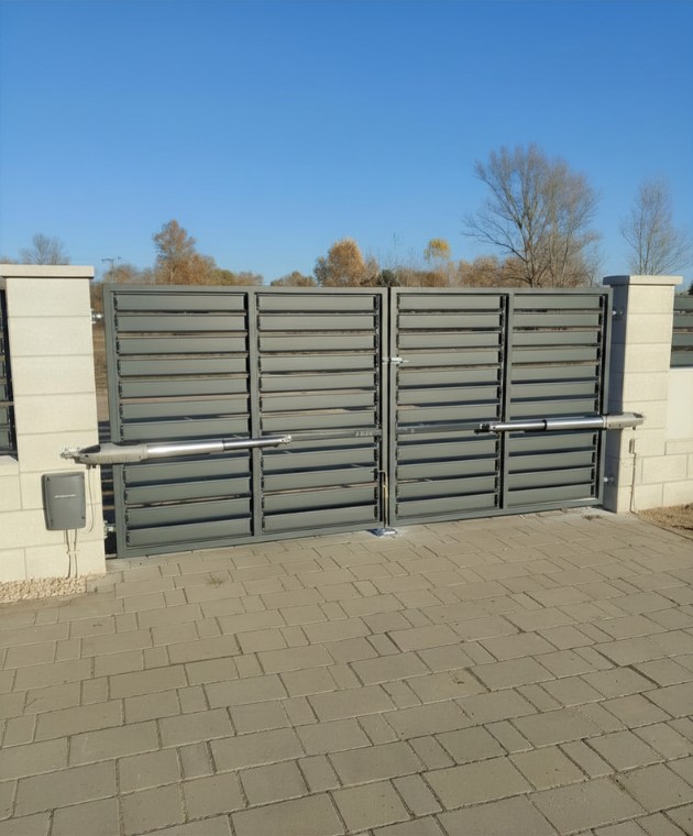 Modern, minimalista stílusú szürke tolókapu és iparikapu automatizálás telephelyen, egyedi méretű beton kerítéselemekkel – Koffenstein Kaputechnika Kft.