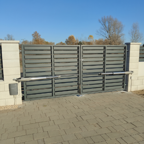 Modern, minimalista stílusú szürke tolókapu és iparikapu automatizálás telephelyen, egyedi méretű beton kerítéselemekkel – Koffenstein Kaputechnika Kft.
